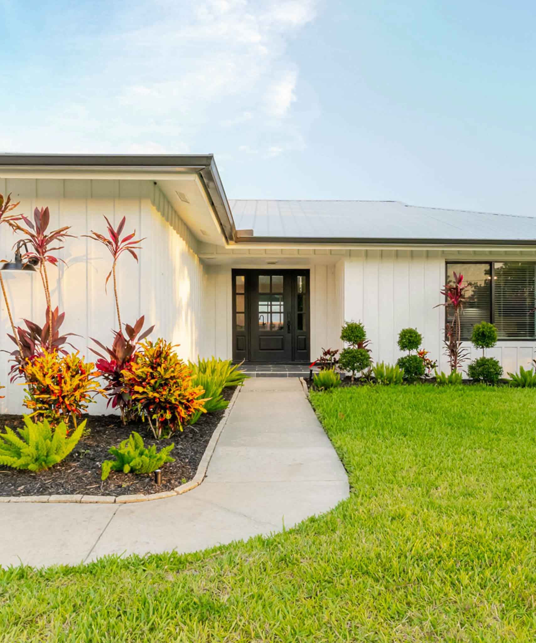 Front view of Coastal Cottage featuring blue skies and manicured lawn and garden.